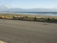 an empty beach road lined with wooden posts and fenced in bench on one side