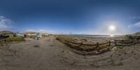 a 360 - fish - eye picture shows the beach and its shoreline with houses and a man walking on it