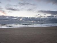 a lone surf board sits on the beach at sunset time and waves wash ashore and