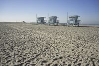 people walk on sand at a beach, near the ocean in the distance is a sky with few cloudless, and blue skies