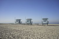 people walk on sand at a beach, near the ocean in the distance is a sky with few cloudless, and blue skies