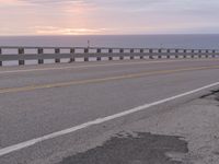 the road is empty with two lane barriers and sun going down to sea in the background