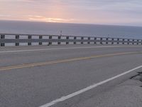 the road is empty with two lane barriers and sun going down to sea in the background