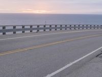 the road is empty with two lane barriers and sun going down to sea in the background