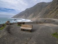 two wooden benches on the ground by the ocean and cliffs with the coast and a sky