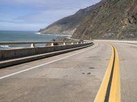 an empty highway next to the ocean with some rocks on it with blue sky in background