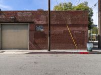 a red fire hydrant sitting next to an empty brick building on a sidewalk and parked cars