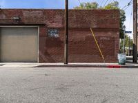 a red fire hydrant sitting next to an empty brick building on a sidewalk and parked cars