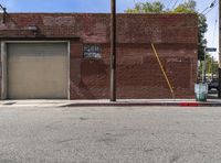 a red fire hydrant sitting next to an empty brick building on a sidewalk and parked cars