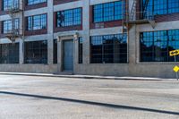 the empty street with a yellow traffic sign in front of an industrial building and another large windows