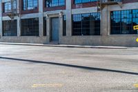 the empty street with a yellow traffic sign in front of an industrial building and another large windows