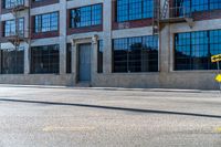 the empty street with a yellow traffic sign in front of an industrial building and another large windows