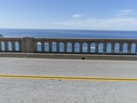 an older couple rides their bicycle on the bridge overlooking the ocean and coastline below a blue sky