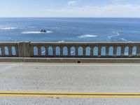 an older couple rides their bicycle on the bridge overlooking the ocean and coastline below a blue sky