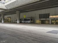 a couple of buses parked in a parking garage next to a sidewalk with concrete pillars