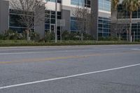 an empty road with some cars parked on it near a building and palm trees in the background