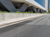 a road next to a building with a lot of windows on it and grass growing up on the side of the road