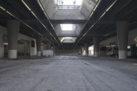 the inside of an empty building looking into an empty parking lot with vehicles parked underneath it