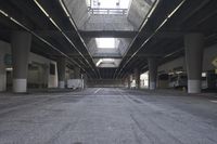 the inside of an empty building looking into an empty parking lot with vehicles parked underneath it