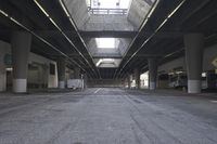 the inside of an empty building looking into an empty parking lot with vehicles parked underneath it