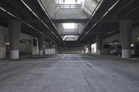 the inside of an empty building looking into an empty parking lot with vehicles parked underneath it