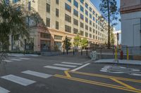 a woman standing at a crosswalk outside a building and a few trees in the foreground