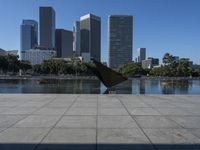 a person with their umbrella on the ground near water and tall buildings behind them in a city