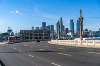 the city skyline stands in a blue sky with clouds over the street and yellow lines on the road