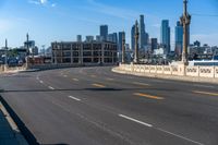 the city skyline stands in a blue sky with clouds over the street and yellow lines on the road