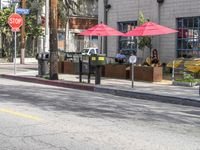 two red umbrellas hang off the poles over the street while two people sit at tables outside the window