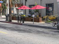 two red umbrellas hang off the poles over the street while two people sit at tables outside the window