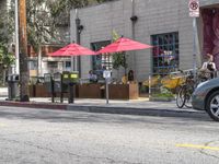 two red umbrellas hang off the poles over the street while two people sit at tables outside the window