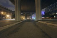 the street under an overpass is empty but there are lights on it at night