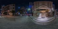 some buildings and a street with lights around it at night time as seen through a fisheye lens