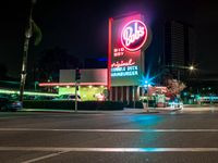 the building next to the street is lit up with neon lights and signs that read dairy