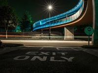 an empty road at night with a blue bridge in the background and text exit only on it