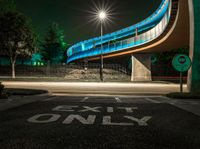 an empty road at night with a blue bridge in the background and text exit only on it