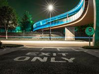 an empty road at night with a blue bridge in the background and text exit only on it