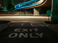 an empty road at night with a blue bridge in the background and text exit only on it