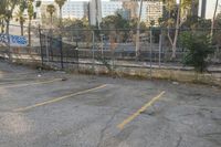 a parking lot with graffiti and trees in the back ground next to the fence and a man walking next to the vehicle