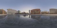 a fisheye photograph of buildings and a pool of water, near a waterfront in downtown