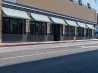 the sidewalk at the corner of the street in front of a building with awnings on one side