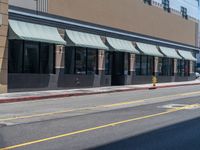 the sidewalk at the corner of the street in front of a building with awnings on one side