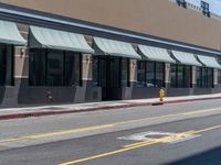 the sidewalk at the corner of the street in front of a building with awnings on one side