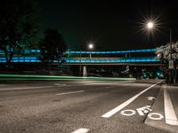 the view of a street from under some lights at night, with two bicycle lanes on the sidewalk