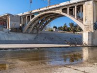 a man is standing near the water under an underpass as a plane approaches by