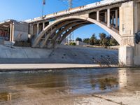 a man is standing near the water under an underpass as a plane approaches by