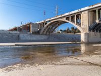 a man is standing near the water under an underpass as a plane approaches by