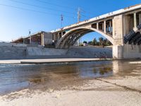 a man is standing near the water under an underpass as a plane approaches by