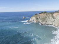 a beautiful cliff and some waves in the water on a clear day from above a hill